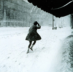 person holding coat closed against blowing wind and snow